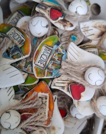Kolekcja malowanych ceramicznych kształtów aniołków, w tym stylizowanych serc, z różnymi wzorami inspirowanymi folklorem i napisem, z których jeden czytelnie brzmi 'MUCZNE'.